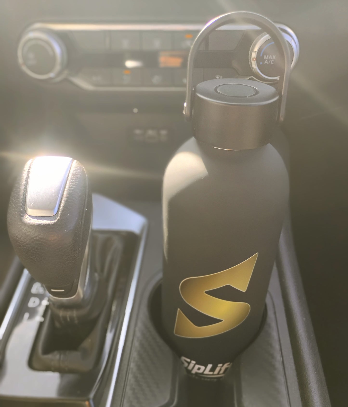 Black water bottle with gold logo on a car's gear shift lever